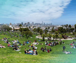 People relaxing on the grass at Dolores Park in San Francisco with city skyline in the background